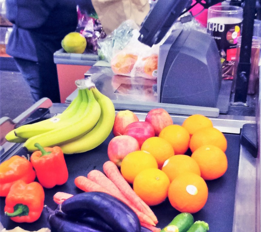 Fruit and vegetables with no bags, on a conveyor belt at a supermarket checkout.