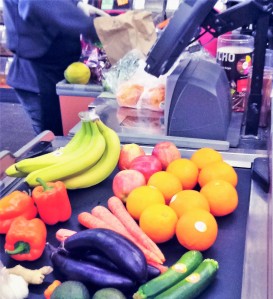Fruit and vegetables with no bags, on a conveyor belt at a supermarket checkout.