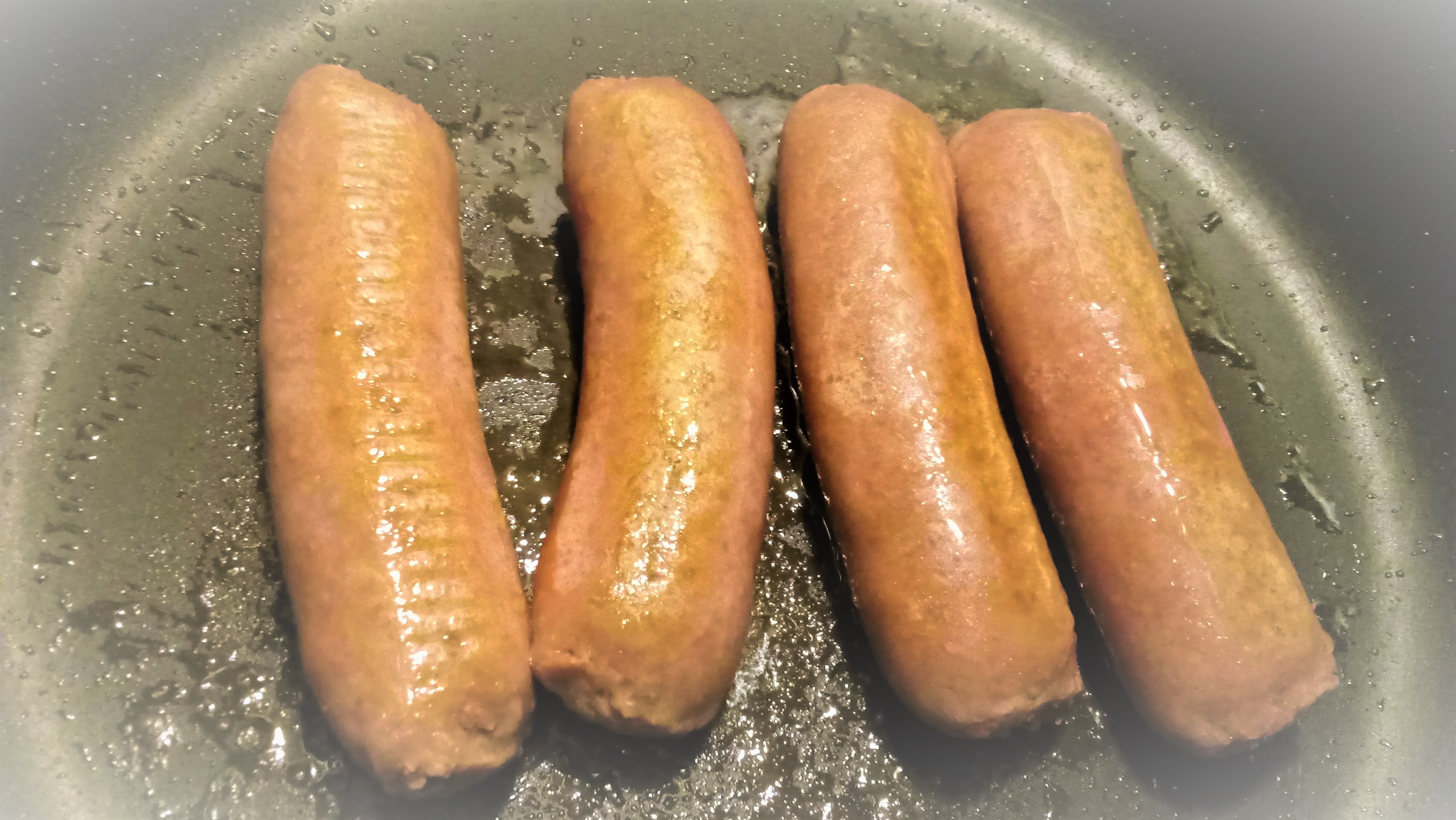 Four Beyond Meat plant-based sausages cooking in a nonstick pan.