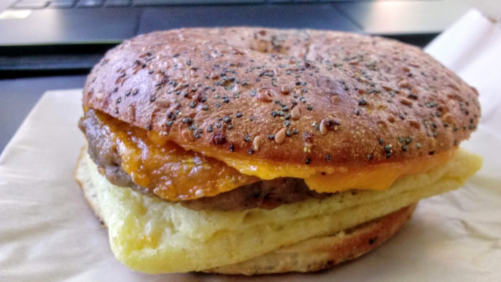 A photo of the Everything Plant-Based Sandwich from Peet's Coffee is shown. The sandwich consists of a sausage patty from Beyond Meat, combined with JUST vegan egg and vegan cheddar, all on a thin everything bagel.