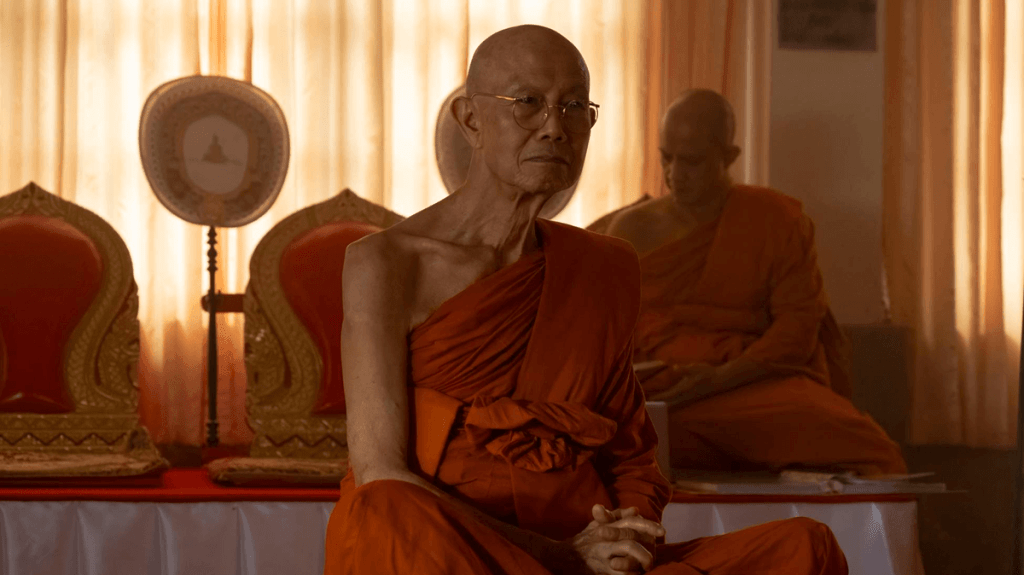 A Buddhist monk, Luang Por Teera (Suthichai Yoon) sitting cross-legged in a scene from The White Lotus, season 3.